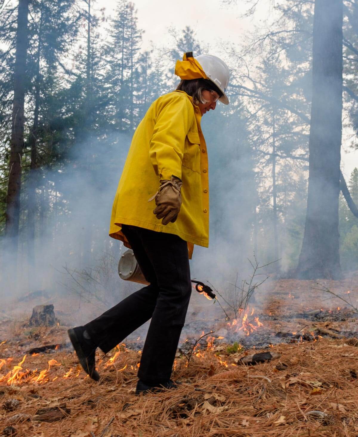woman in fire proof gear walking through the forest doing a controlled burn