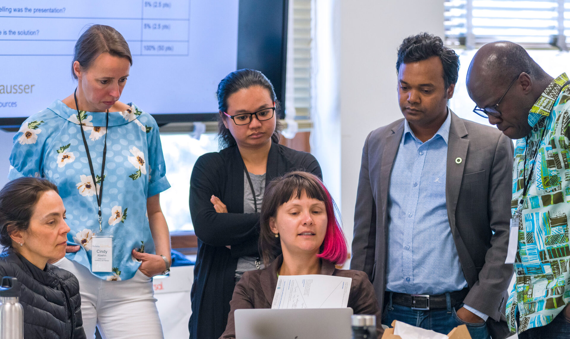 Six Beahrs ELP fellows working on a project in a Berkeley classroom, with one woman pointing to a laptop screen and the others listening to her, as an example of a classroom environment similar to the Master of Climate Solutions