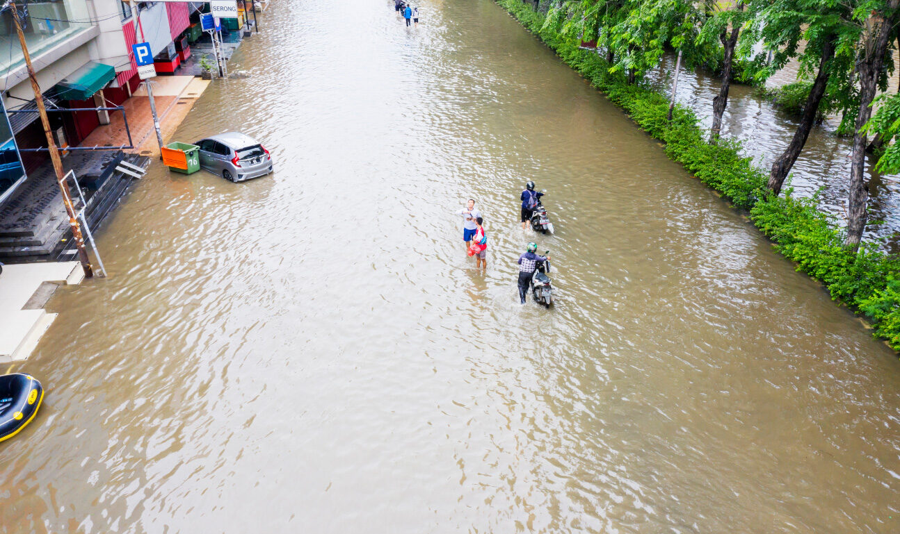 A flooded road with people, cars, and motorcycles in the flood, illustrating a climate crisis.