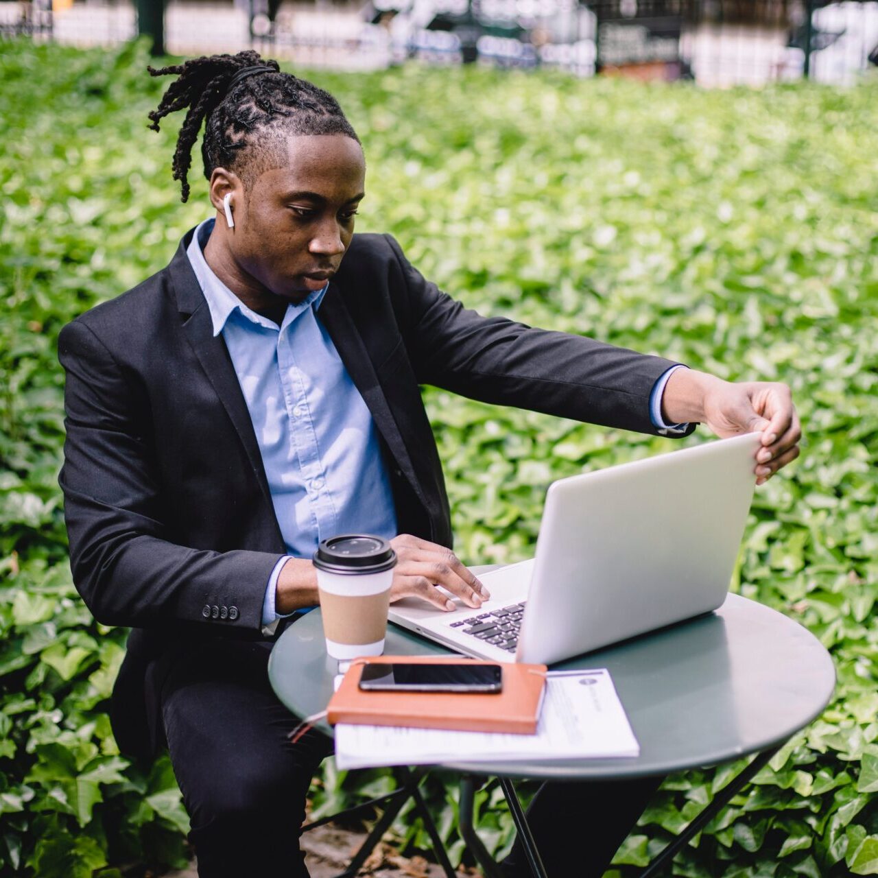 Man in business suit at a small table with a laptop in front of a shrub